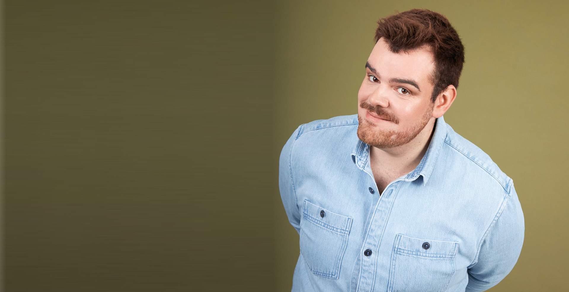 Ein Mann mit blauem Hemd steht vor einem grünen halbschattierten Hintergrund.